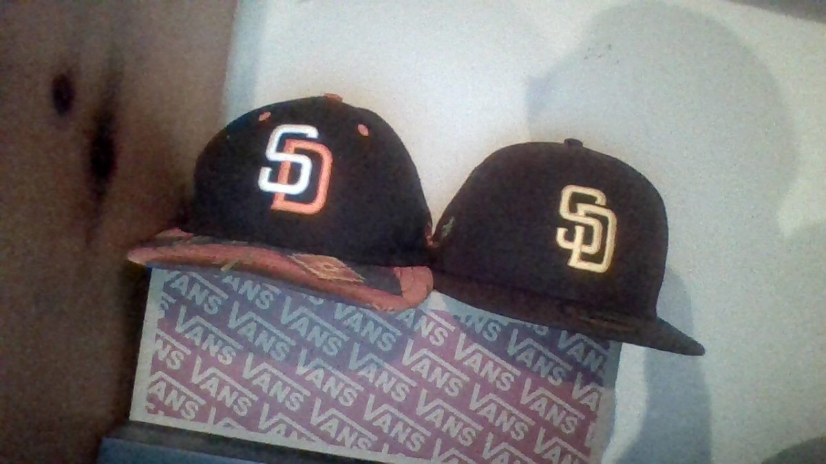 Two San Diego Padres hats placed together on a shoe box. The hat to the left used to be Miguel Rosas Brothers hat and the one on the right was bought for him after graduating 8th grade by his dad.