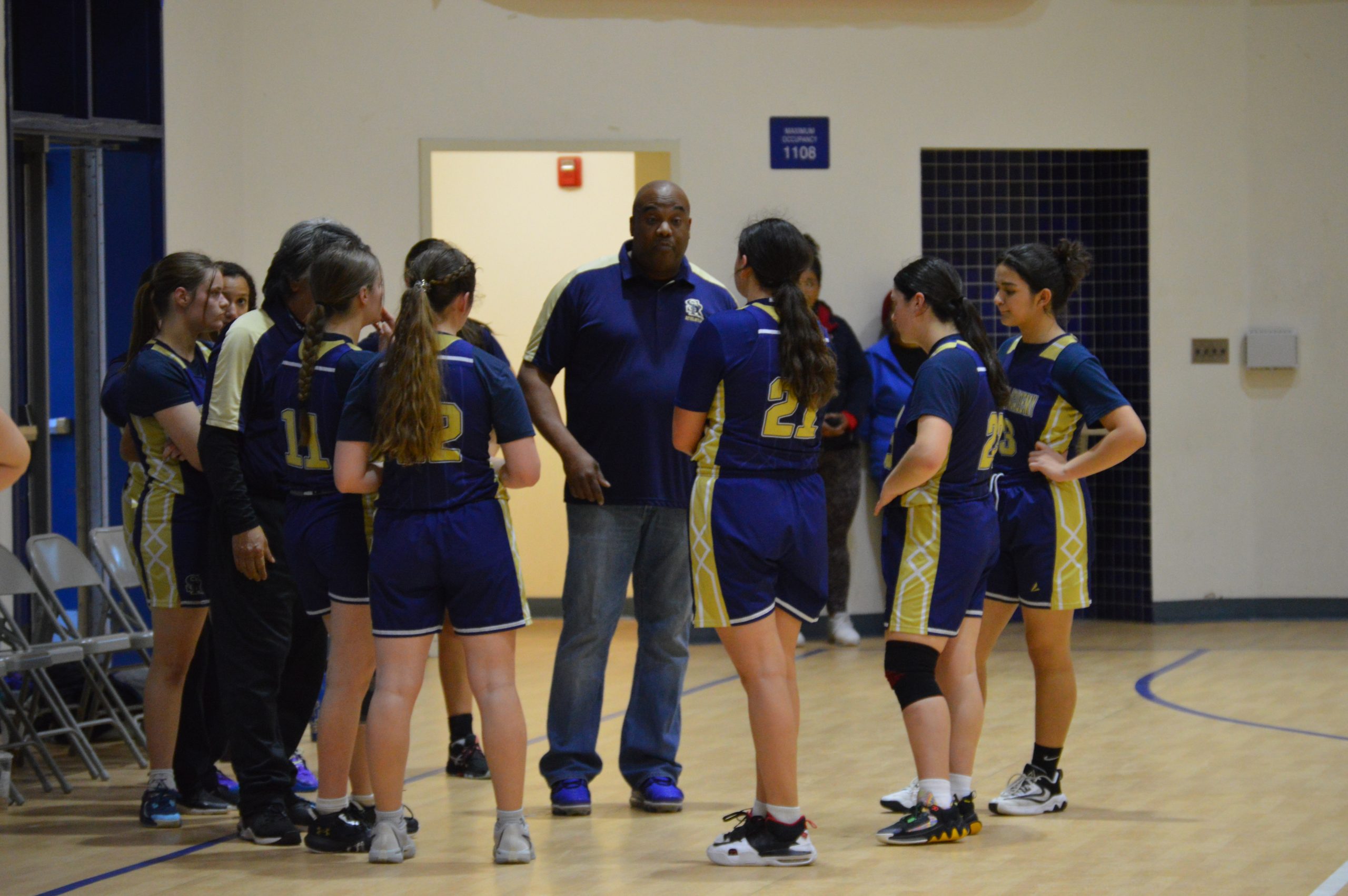 Coach Walter Garland talks to the girls' 2023-2024 basketball team in the last league game. It was a close game and Coach gave words of motivation to finish the game strong. He plans on passing this motivation down to the new girls.