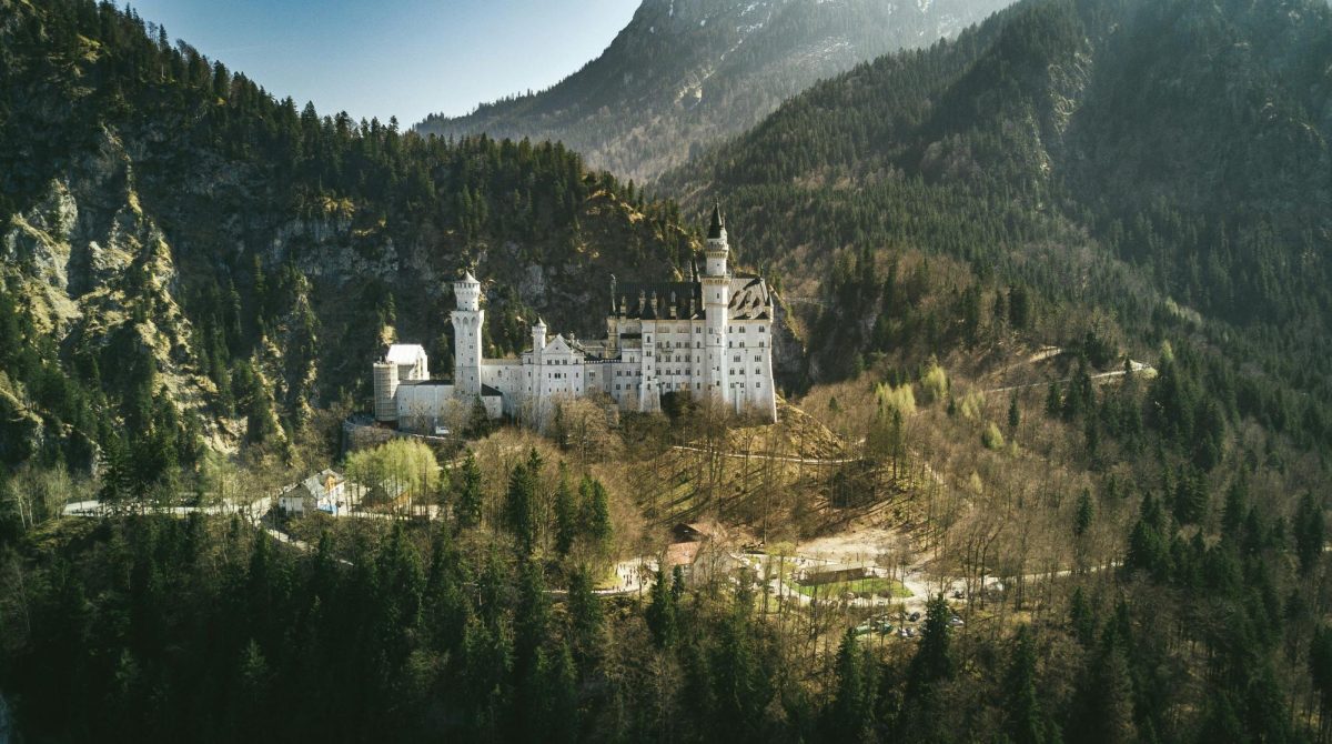 Landscape of Neuschwanstein Castle in Schwangau, Germany. It is surrounded by a pine forest with hills and mountains.