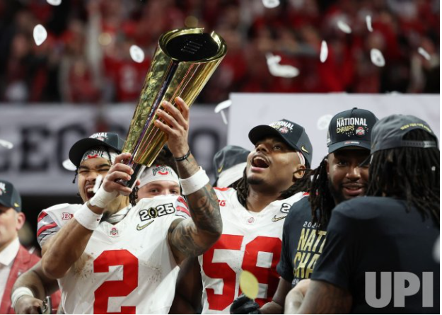 Emeka Egbuka holding up the National Championship Trophy. Ohio State football team celebrating in the background.