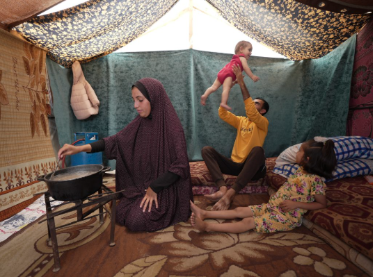 The photograph shows a Palestinian family in a refugee camp in Gaza attempting to make the best of a bad situation. As the rationing and now starvation increases many cannot eat.